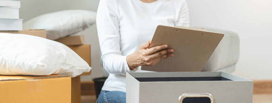 Happy woman checking stuff in cardboard box before sent to transportation company and moving to new location apartment.