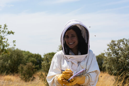 Woman beekeeper wearing bee suit writing notes