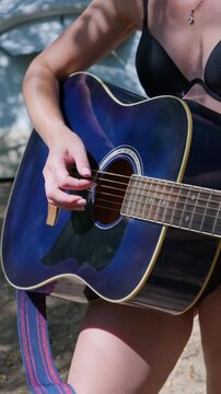 A woman plays chords on a blue acoustic guitar with a colorful strap outside. Concept of summer leisure, acoustic music hobby, authentic lifestyle, and creative musical performance.
