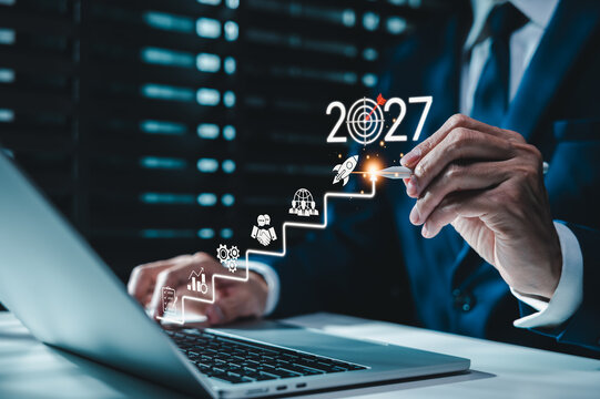2027 business growth strategy and goal achievement concept. Businessman using laptop, roadmap, target, rocket and rising steps, representing planning, innovation, leadership, progress, future success