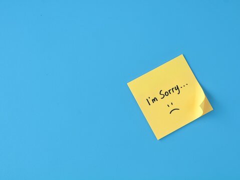 Handwritten I'm sorry message with sad face on yellow adhesive note placed on blue background with copy space. Concept for apology, regret, forgiveness, empathy, relationship, and office communication