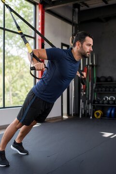Man performing suspension strap chest press in gym. Athletic male doing bodyweight training with TRX equipment. Strength and conditioning concept
