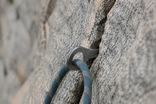 A steel climbing piton in granite with a rope, natural daylight.