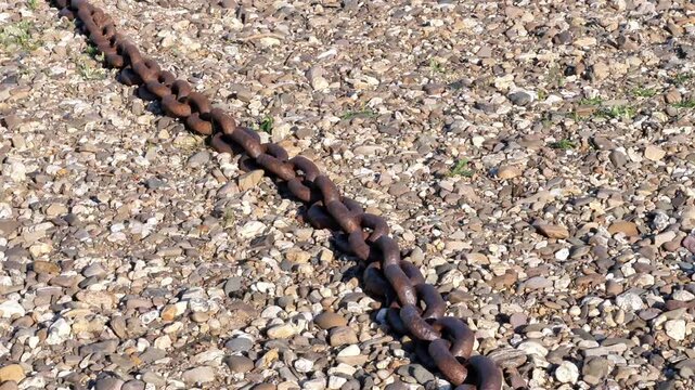 Heavy rusted anchor chain lying on a gravel and pebble shore