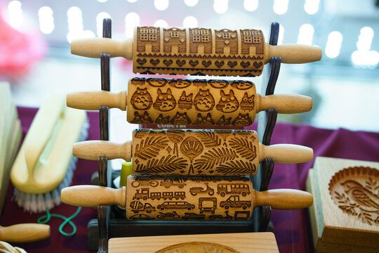 Set of four engraved wooden rolling pins in a metal rack beside a carved cookie stamp at a craft market, ready for handmade baking and artisan kitchenware retail content