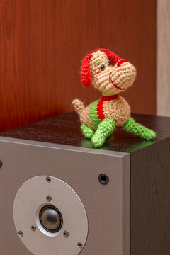A knitted wool dog stands on a speaker.