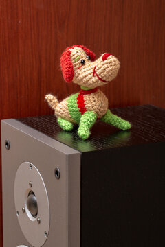 A knitted wool dog stands on a speaker.