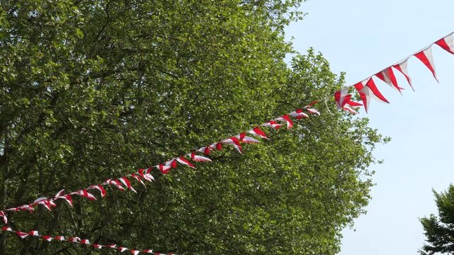 Red and white festive bunting flags hanging against green trees on a sunny day