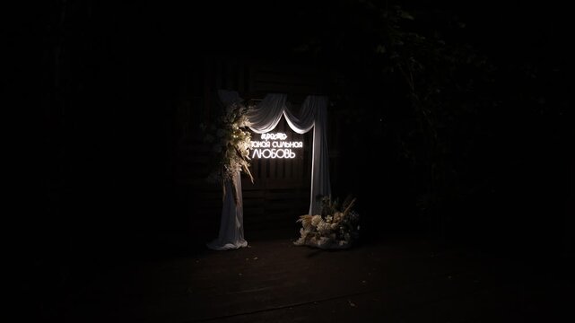 illuminated wedding arch at night in a dark outdoor setting with elegant and celebratory atmosphere, featuring fabric and wooden structure elements, static camera angle.