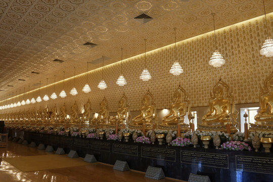 oriental temple interior featuring a perspective row of seated golden buddha statues ornate patterned ceiling crystal chandeliers and glossy wooden floors