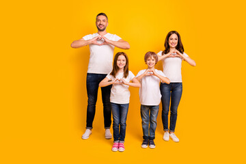 Fototapeta premium Happy family portrait with parents and two children making heart hands on bright yellow background, casual clothing and smiling together to show love and unity