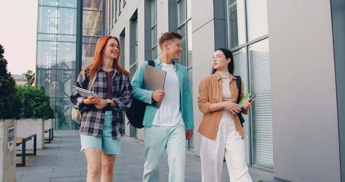 Group of happy young male and female students walking together on the university campus. Diverse college friends laughing and enjoying their time