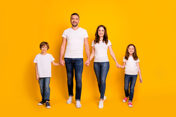 Obraz premium Happy family of four holding hands and smiling against a bright yellow background, parents with two children in casual white t-shirts and jeans