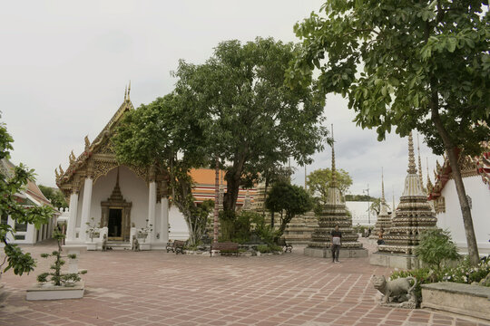 lush courtyard garden with shade trees, traditional thai temple pavilions, and ornate mosaic stupas at wat pho in bangkok