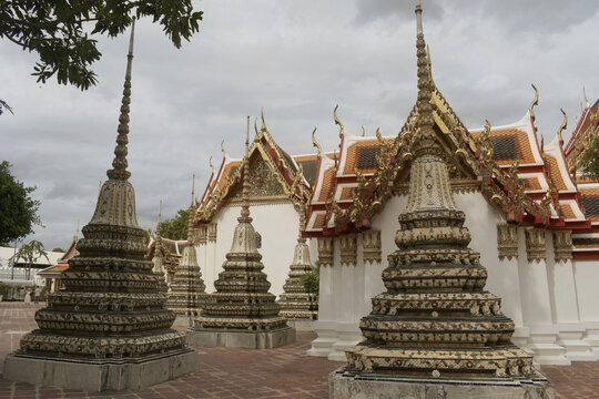 rows of decorative ceramic tiled chedi stupas standing in stone courtyard beside ornate ordination hall at 'wat pho', bangkok, thailand