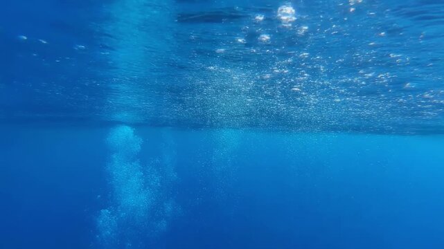 Bubbles ascending in clear blue ocean water during daylight with gentle underwater movement