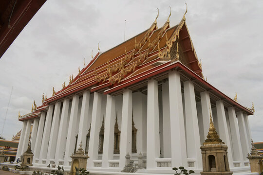 exterior perspective of the massive phra ubosot ordination hall featuring tall white colonnade pillars and tiered orange roof at wat pho temple of the reclining buddha, bangkok, thailand 