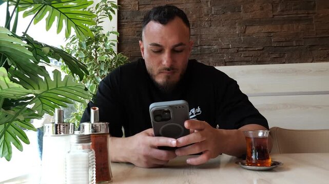 Focused young man sitting in a cafe using his smartphone and drinking tea
