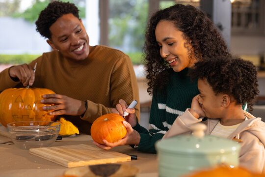 African American family carving pumpkins at kitchen table with carving tools and marker