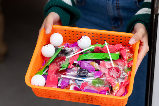 African American woman holding orange basket with candy lollipops white balls in sweater at doorway