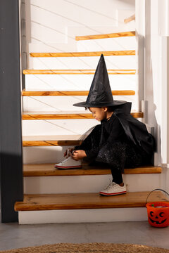 African child sitting on stairs tying sneaker in pointed witch hat with jack o lantern nearby