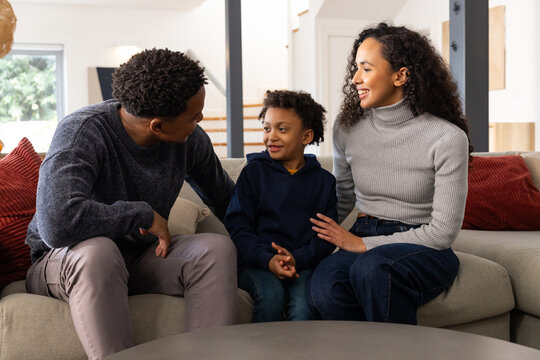 African American family sitting closely on light-gray sofa in living room, man leaning toward child