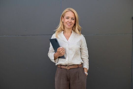Confident blonde businesswoman holding digital tablet smiling