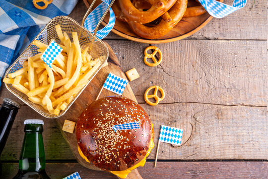 Oktoberfest Burger menu with french fries, pretzels, beer bottles. Tasty cheese hamburger in pretzel bun, with french fries, bavarian beer snacks, with checkered tablecloth and Oktoberfest decor