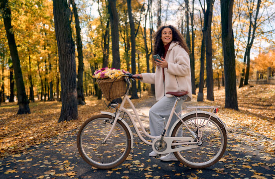 Woman cycling with flowers through autumn park.