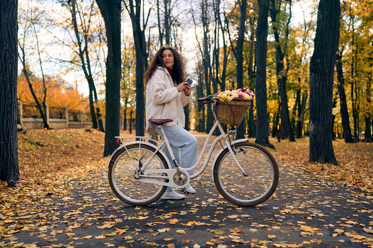 Woman with flower basket bicycle in autumn park.