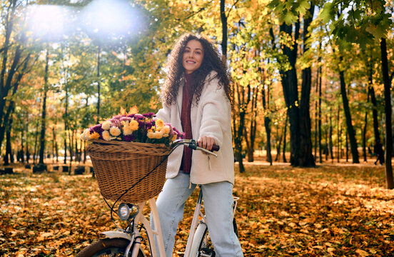 Woman riding a flower basket bicycle in an autumn park.