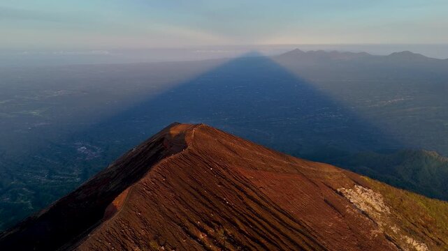 Aerial view of Mount Agung casting a long triangular shadow over the landscape in Rendang, Bali, Indonesia.