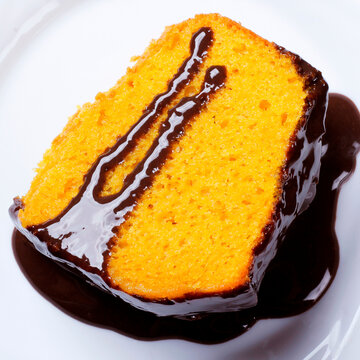 Slice of Brazilian carrot cake with glossy chocolate frosting on a white plate.
