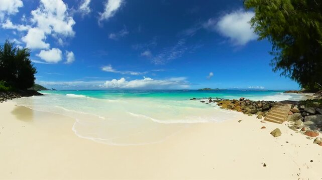 Quiet beach with crystal-clear water, rock formations, and lush greenery under a deep blue sky. Seychelles, Praslin.