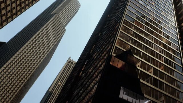 Two tall buildings reach up toward the sky in a city. The view is from the ground, showing the details of the structures and the blue sky above.