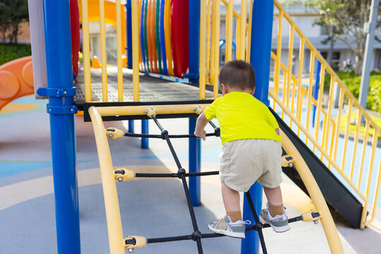 Toddler boy climbing up rope net structure at outdoor playground