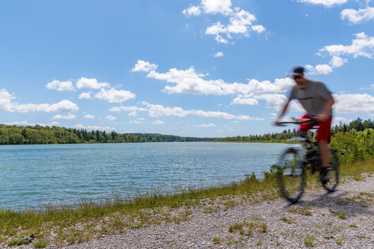 Motion blurred cyclist riding mountain bike along scenic lake shore under blue sunny sky, active lifestyle and outdoor sports concept