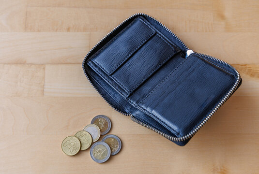 Open empty black leather wallet with small stack of euro coins on wooden table, inflation and personal finance concept
