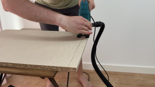 A man adjusts the blade guard of an electric jigsaw while cutting a shelf