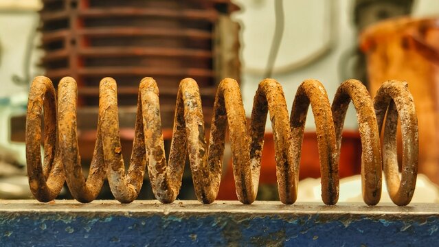 Rusty coiled spring metal on a weathered surface with industrial background
