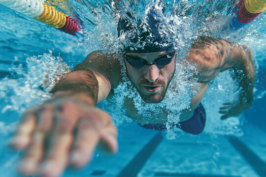 A male swimmer in a blue cap and goggles, actively swimming freestyle underwater.