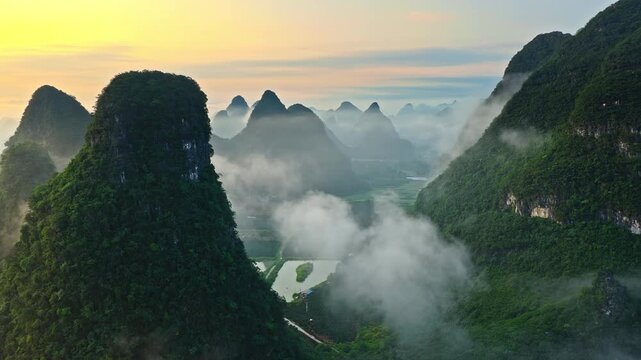 Aerial drone view of a misty sunrise over green karst mountain peaks with fog floating in the valley of Guilin, China.