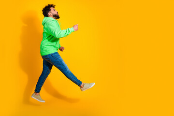 Obraz premium Young man jumping in a green hoodie against a bright yellow background, energetic casual motion and joyful expression in studio portrait