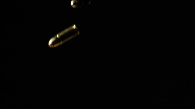 Multiple handgun bullets falling against black background in slow motion.