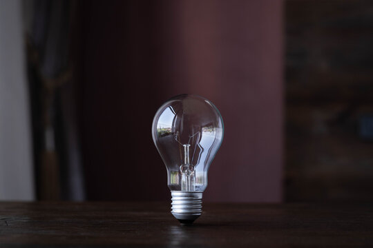 Clear incandescent light bulb on a wooden table with dark background and copy space, symbolizing bright ideas, innovation, creativity, energy, electricity, inspiration, and minimalist design.