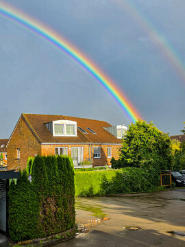 bright rainbow over a suburban brick house and green garden after a summer rain shower