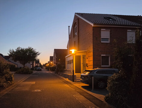 quiet residential street with brick houses and glowing streetlight at blue hour