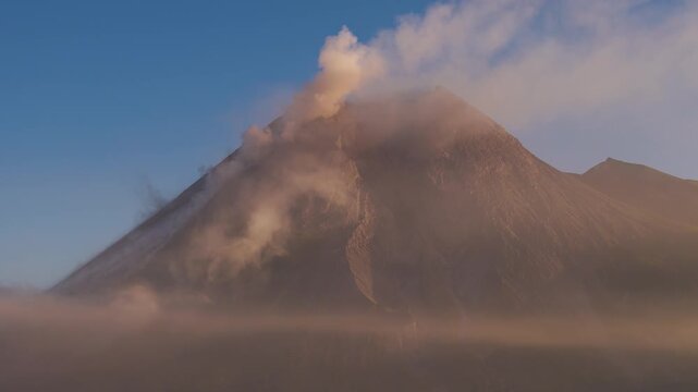 Aerial view of Mount Merapi volcano with volcanic smoke rising into the sky at sunrise in Cangkringan, Special Region of Yogyakarta, Indonesia.