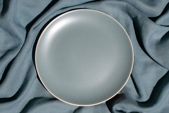 Empty ceramic plate on rumpled grey blue linen cloth, featuring a matte finish and soft tactile textures for artisan tableware and food branding mockup