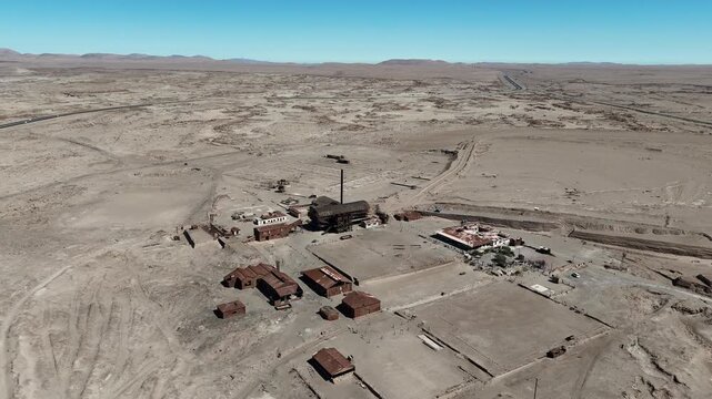 Aerial video of the abandoned Humberstone saltpeter refinery, a UNESCO World Heritage site featuring a tall chimney in the Chilean desert.